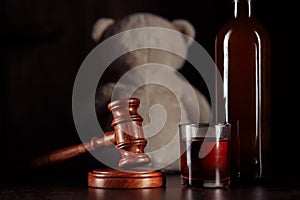 Alcohol in family and child abuse concept. Teddy bear as a symbol of child`s safety, judge gavel and bottle with glass