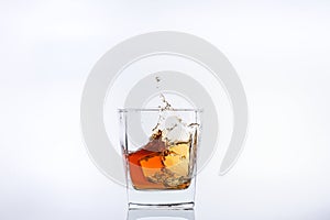 Alcohol in the glass. Ice cube falls into a glass with splashes. Isolated on white background.