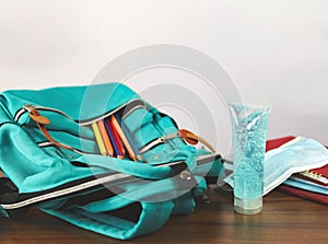 Alcohol sanitizer hand gel, medical face mask, school backpack with school supplies on wooden table on white background
