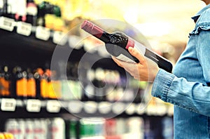 Alcohol shelf in liquor store or supermarket. Woman buying a bottle of red wine and looking at alcoholic drinks in shop.