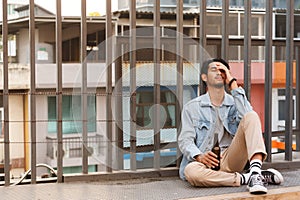 Alcoholic asian man drink beer from the bottle sitting on the floor after party. Sad heartbroken young man holding beer bottle in