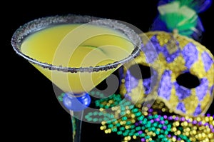 Alcoholic beverage and pourple, green and gold Mardi Gras beads with mask on a black bckground for a festive February holiday