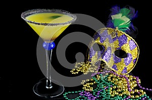 Alcoholic beverage and pourple, green and gold Mardi Gras beads with mask on a black bckground for a festive February holoiday ima