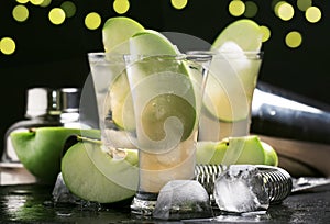 Alcoholic cocktail with dry white vermouth, green apple, juice, soda and ice, black bar counter background, selective focus
