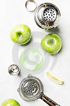 Alcoholic cocktail with green apple and dry vermouth, syrup, lemon juice and ice cubes. Bar tools, gray stone background, top view