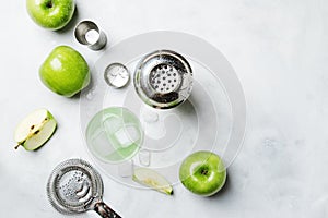 Alcoholic cocktail with green apple and dry vermouth, syrup, lemon juice and ice cubes. Bar tools, gray stone background, top view