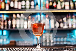 An alcoholic cocktail of red color with a decoration of lemon peel stands on a bar counter.