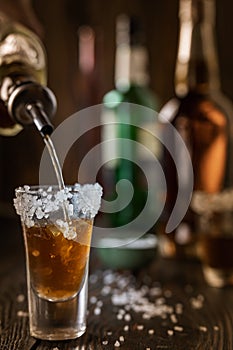 An alcoholic drink at the bar counter is poured into a tequila glass with salt at the edges, in the background are