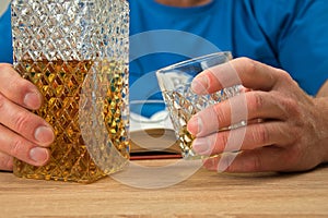 Alcoholic drink in crystal decanter. Man holds in his hand a glass with a drink of whiskey. Open book with glasses