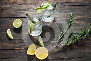 Alcoholic drink gin tonic cocktail with lemon, rosemary and ice on rustic wooden table.