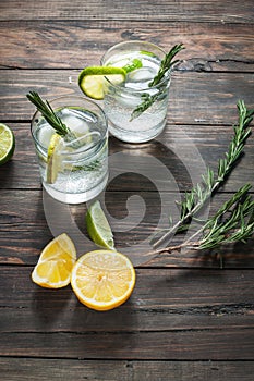 Alcoholic drink gin tonic cocktail with lemon, rosemary and ice on rustic wooden table.