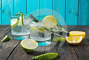 Alcoholic drink gin tonic cocktail with lemon, rosemary and ice on rustic wooden table