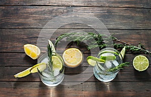 Alcoholic drink gin tonic cocktail with lemon, rosemary and ice on rustic wooden table, copy space.