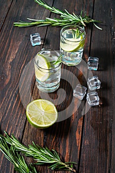 Alcoholic drink - gin tonic cocktail - with lime, rosemary and ice on rustic wooden