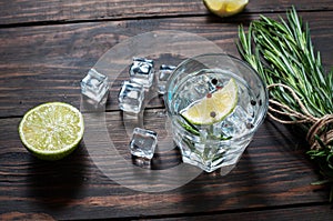 Alcoholic drink - gin tonic cocktail - with lime, rosemary and ice on rustic wooden table