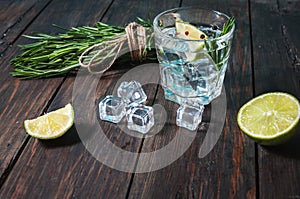 Alcoholic drink - gin tonic cocktail - with lime, rosemary and ice on rustic wooden table