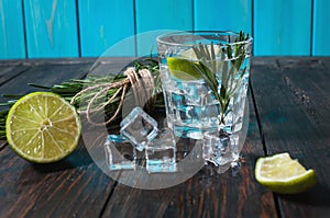 Alcoholic drink - gin tonic cocktail - with lime, rosemary and ice on rustic wooden table