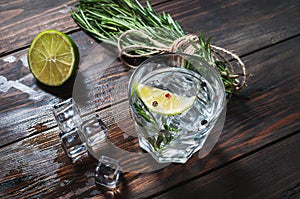 Alcoholic drink - gin tonic cocktail - with lime, rosemary and ice on rustic wooden table