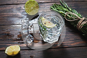 Alcoholic drink - gin tonic cocktail - with lime, rosemary and ice on rustic wooden table