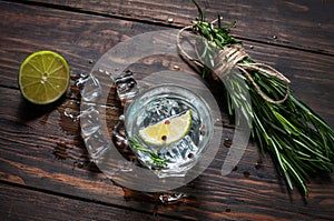 Alcoholic drink - gin tonic cocktail - with lime, rosemary and ice on rustic wooden table