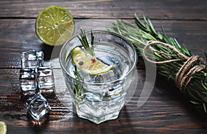 Alcoholic drink - gin tonic cocktail - with lime, rosemary and ice on rustic wooden table