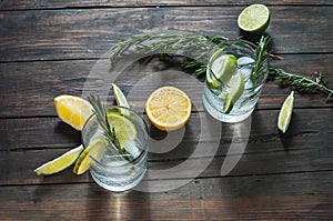 Alcoholic drink with lemon, rosemary and ice on rustic wooden table