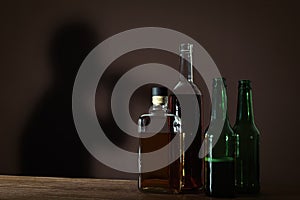 Alcoholic drinks on wooden table against brown wall with shadow of addicted man