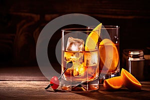 Alcoholic old fashioned cocktail with orange slice, cherry and orange peel garnish