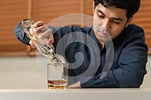 Alcoholism, depressed asian young man pouring, holding bottle whiskey into the glass, drinking alcohol beverage at night.