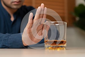 Alcoholism, depressed asian young man refuse, push out alcoholic beverage glass, drink whiskey, sitting alone at night. Treatment