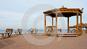 Alcove and benches on the beach. Big wooden alcove and two benches on sand shore. Empty place for meeting near sea.