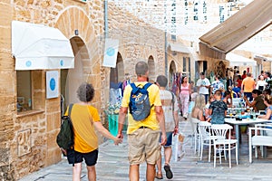 ALCUDIA, SPAIN - July 8, 2019: Restaurant tables on street with tourists in seaside Alcudia old town, Mallorca island