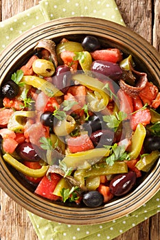 Algerian salad Chlada felfel with green pepper tomato, anchovies and mix of olives close-up in a bowl. vertical top view