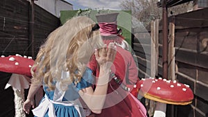 Alice and the Hatter from Alice in Wonderland look into the camera. They ask not to make noise putting fingers to a mouth and then