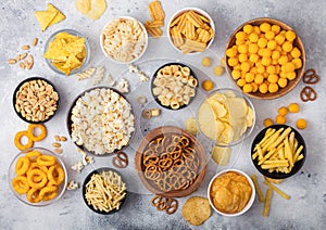 All classic potato snacks with peanuts, popcorn and onion rings and salted pretzels in bowl plates on light background. Twirls