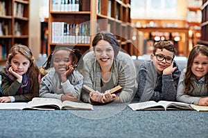 All great leaders started by reading. elementary school kids reading with their teacher on the floor in the library.