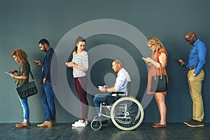 We all have the same phone. Shot of a group of people standing in a row behind each other while using their phones.