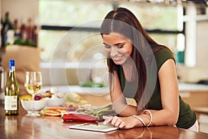 All her recipes on one device. Shot of an attractive young woman using her tablet to look up a recipe in her kitchen.