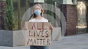 ALL LIVES MATTER concept, no racism. Outdoors portrait of a young female activist wearing a medical mask holding a