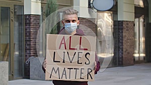 ALL LIVES MATTER concept, no racism. Outdoors portrait of a young male activist wearing a medical mask holding a