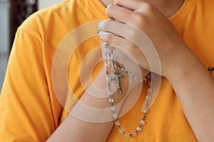 With all of my heart. Junior woman hands holding The Rosary with Jesus Christ holy cross crucifix on her chest, close to the heart