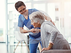 We all need a hand from time to time. a young female nurse helping her senior patient up from a chair in the old age