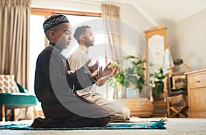 We all need a prayer circle. a young muslim man and his son praying in the lounge at home.