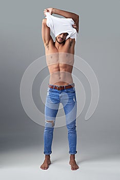 All he needs is jeans. Studio shot of a handsome young man undressing against a grey background.