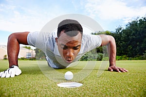 All it needs is a little bit of help. a handsome man trying to blow his golf ball into the hole.