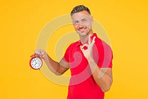 All right. Happy man hold alarm clock showing OK sign. Punctuality and accurate timekeeping. Chronometry and timekeeping