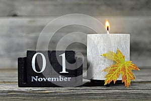 All Saints Day. Burning candle, wooden calendar and yellow autumn leaf