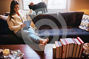 All set for a purrfect sofa day. an attractive young woman using a digital tablet on the sofa and affectionately