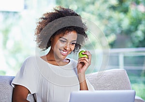 All this surfing is giving me an appetite. a young woman eating an apple and surfing the net.