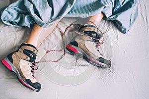 All time ready for trekking. Hiker female sleeping in comfort trekking boots. Footwear on the bed sheet background concept image.